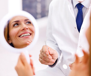patient smiling in reflection of handheld mirror with doctor
