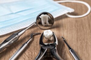 Forceps holding extracted tooth that's reflected in dental mirror next to mask